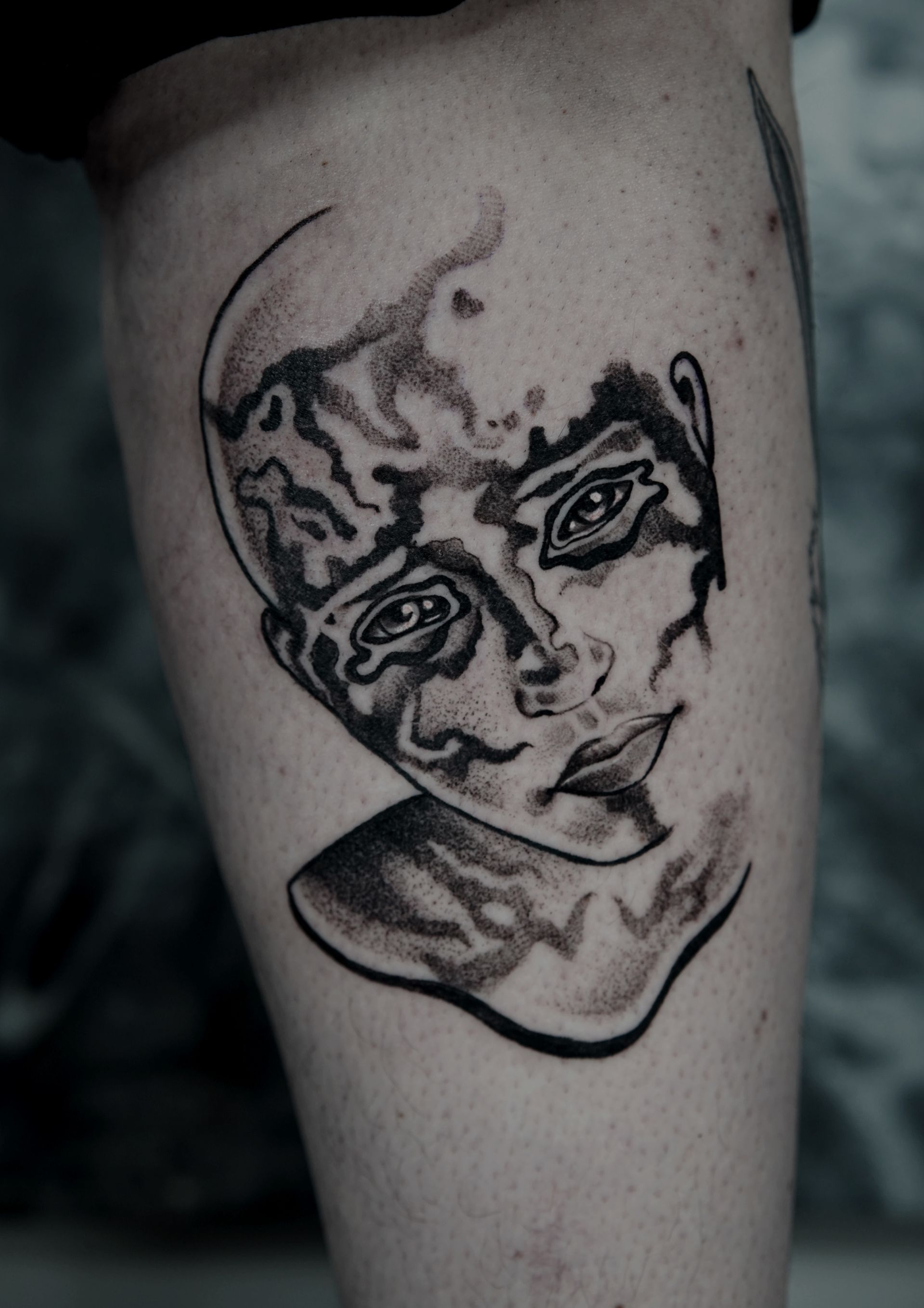 Black ink tattoo of a child's face, with a surreal, melting effect, on a leg.