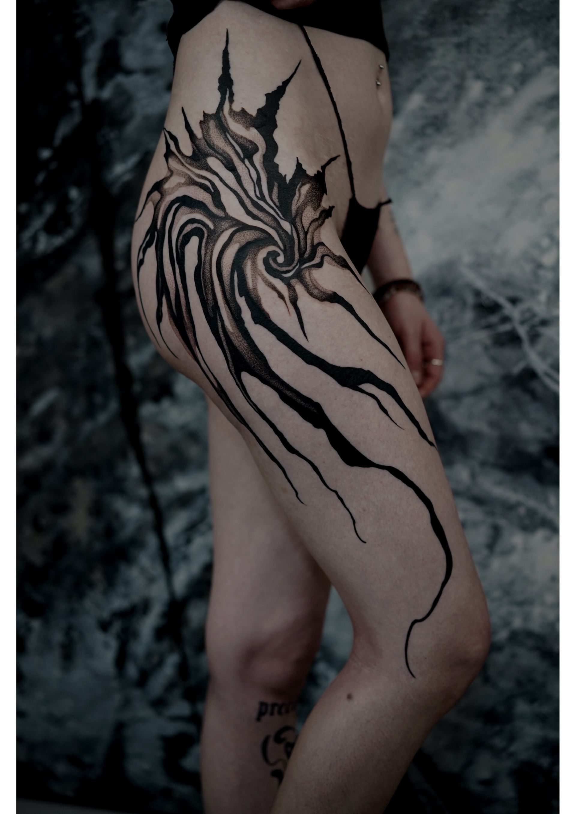 Tattoo on upper leg and hip: swirling black abstract design. Person in dark clothing.