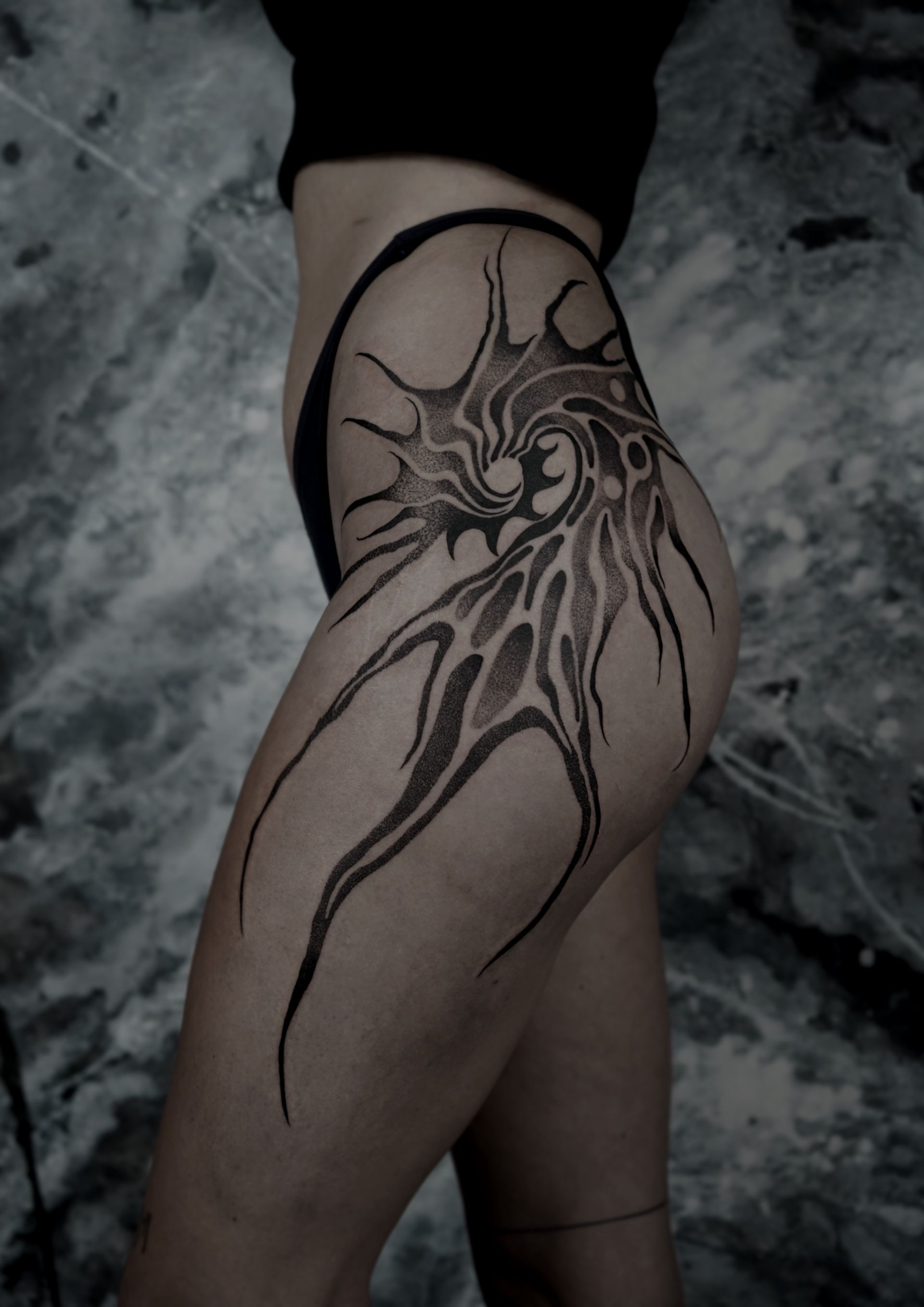 Person's hip and thigh with an abstract black tattoo in a swirling, organic design.