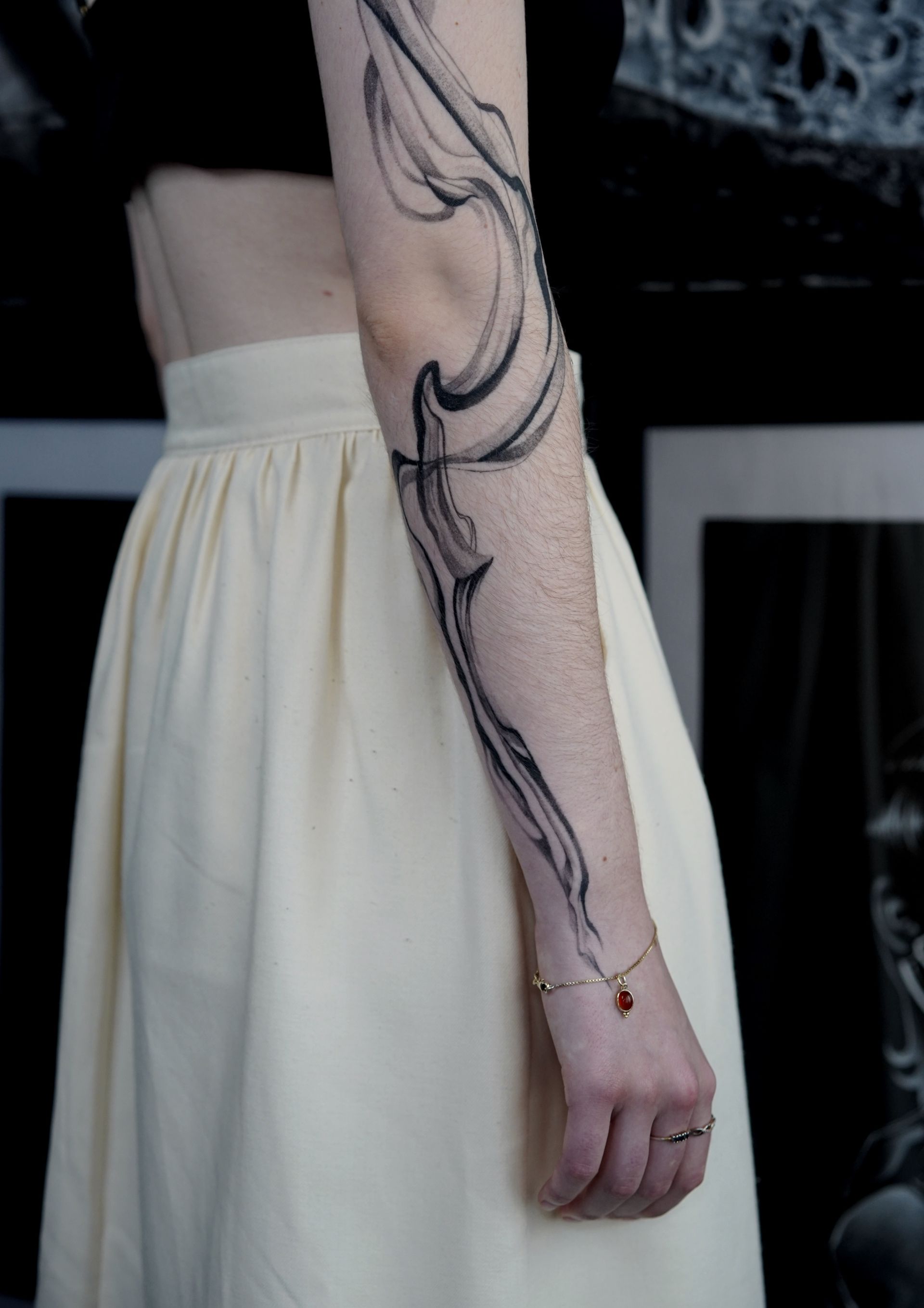 Person with a cream skirt and an arm tattoo in abstract black ink.