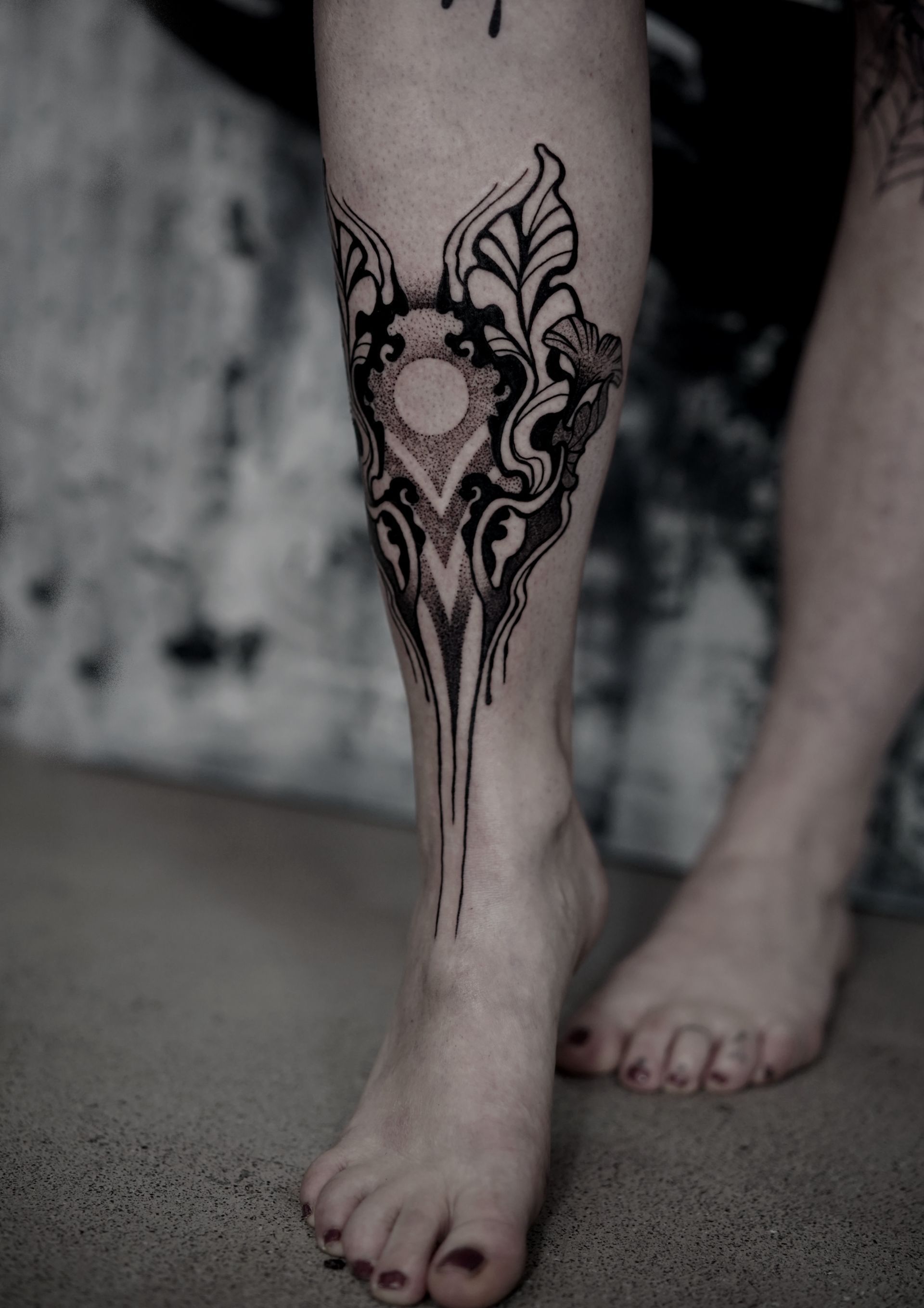 Black henna tattoo on a person's leg, featuring intricate floral and geometric patterns.