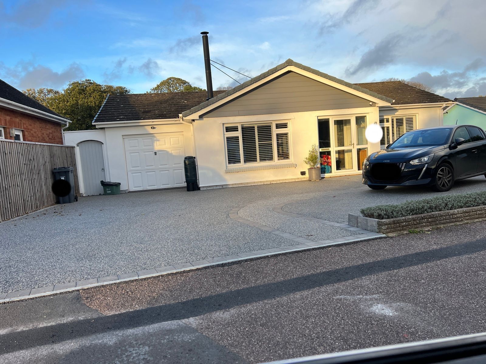 Bungalow with gravel driveway, car parked in front. White exterior, shuttered windows, and a gray roof.