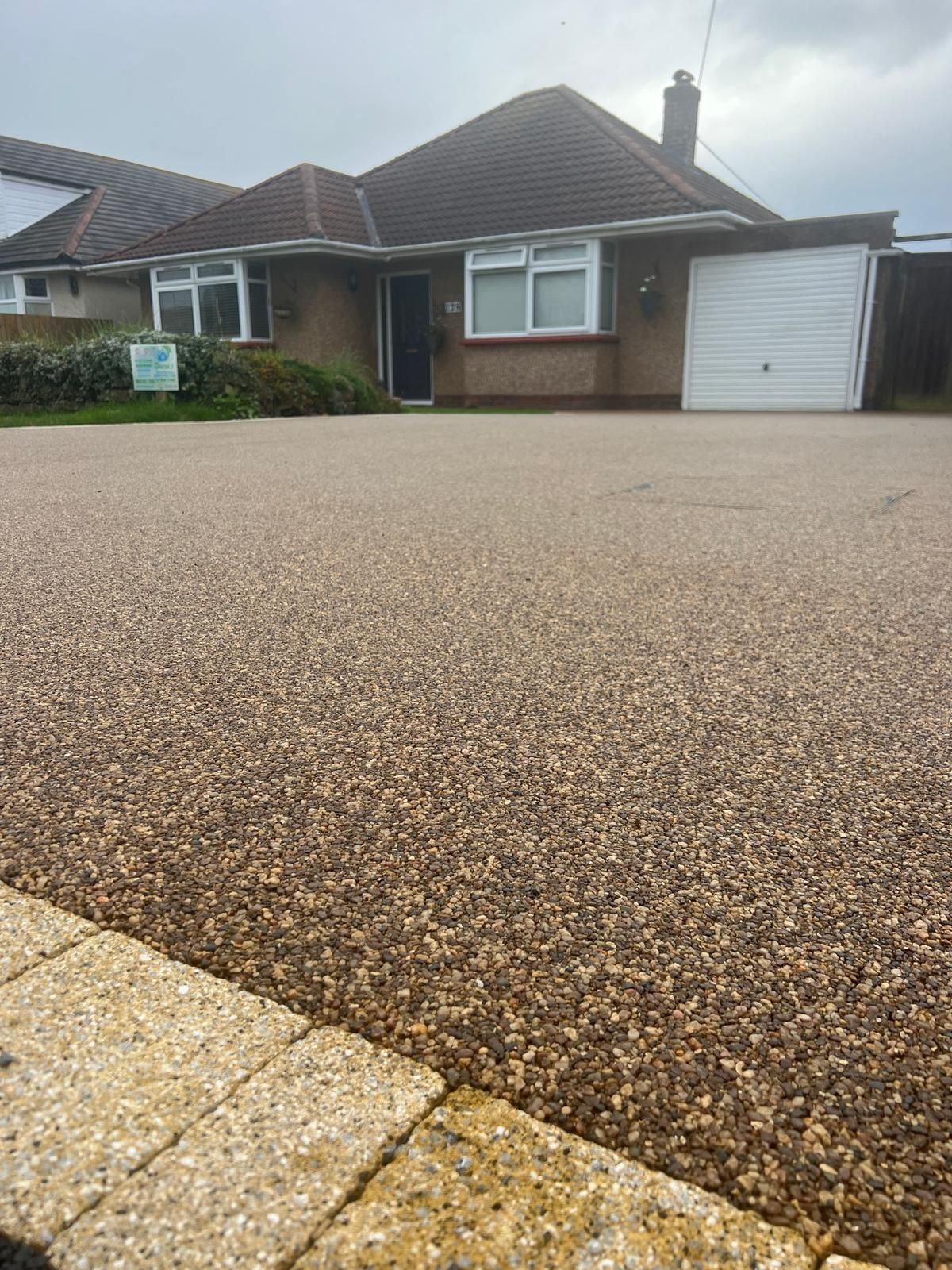 A gray gravel driveway with a green fence in the background.