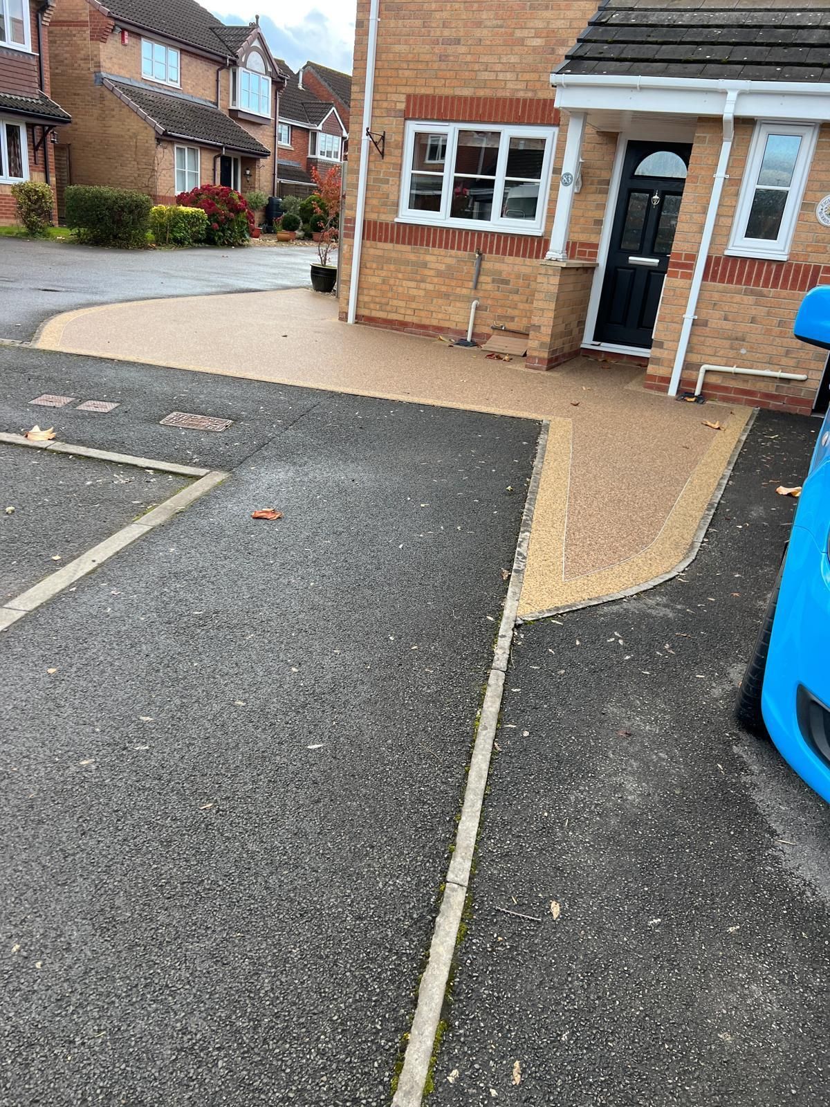 A blue car is parked in front of a brick house.