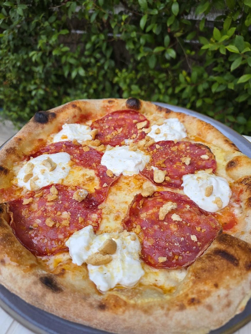 Pizza al salame piccante con ciuffi di formaggio bianco su un tagliere di legno all'aperto