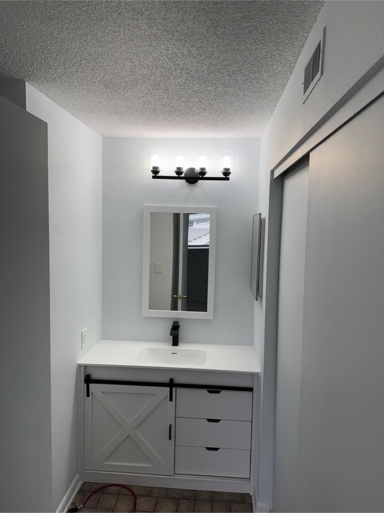 Narrow white bathroom with vanity, mirror, and overhead light above a sink.