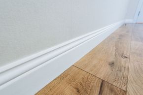 White baseboard and textured wall beside light wood flooring in a hallway