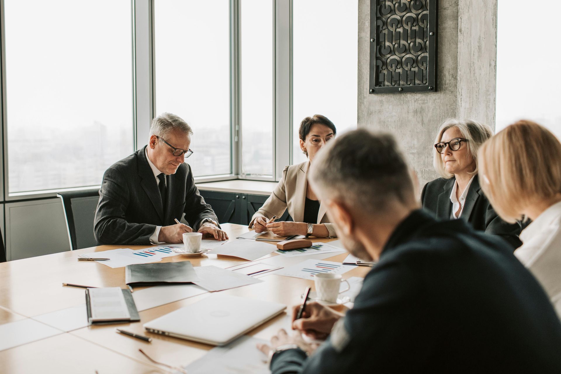 Businesspeople in a conference room, reviewing documents, sitting around a table with a city view backdrop.