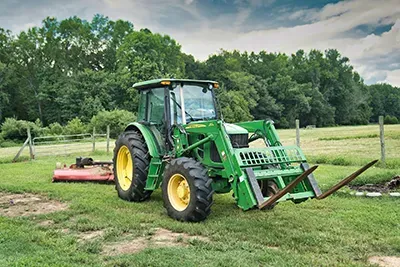 Green John Deere tractor with front forks, in a grassy field.