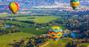 A group of hot air balloons are flying over a lush green valley.