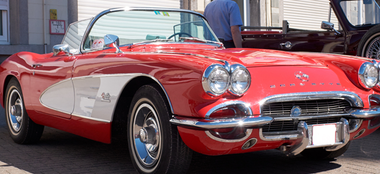 a red and white corvette convertible is parked in front of a building .