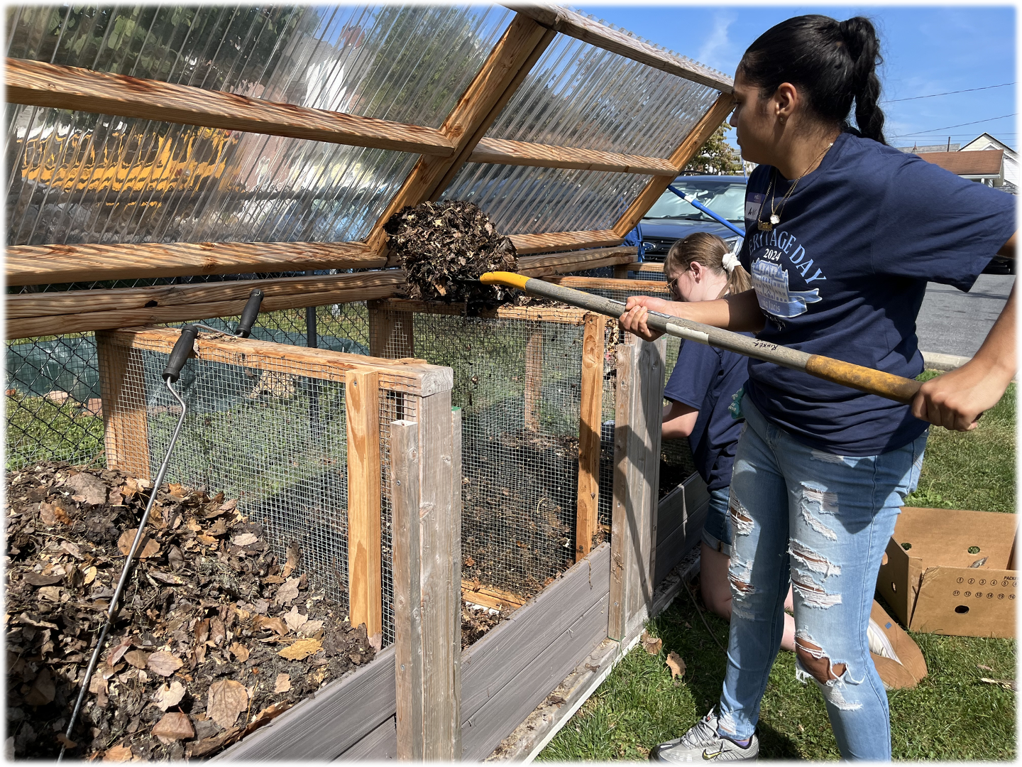 Person raking leaves in a garden bed with wooden frame and clear cover.