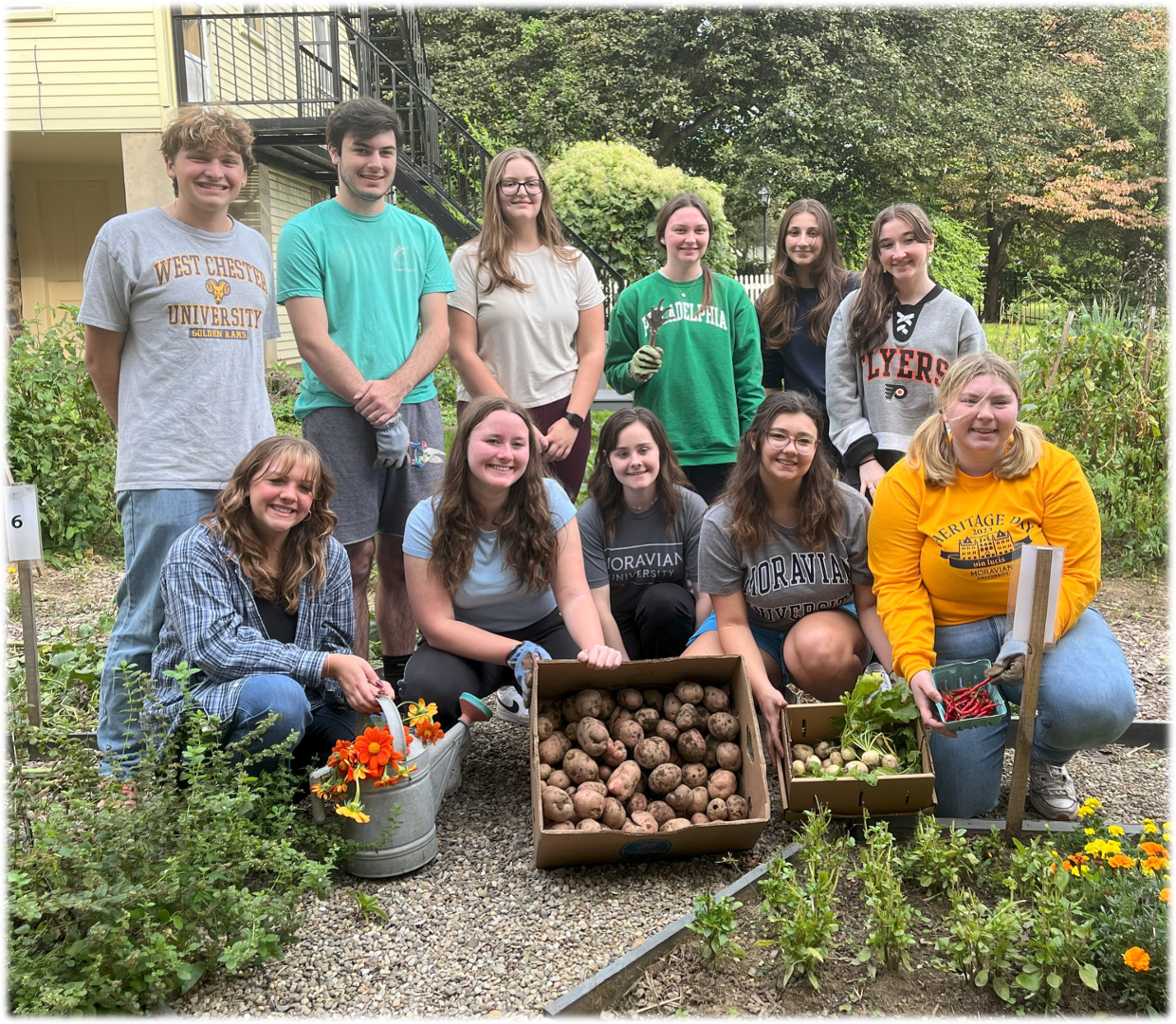 Group of young people harvesting vegetables in a garden, smiling. They hold potatoes and other produce.