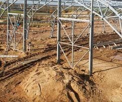 Struttura in acciaio di un edificio in costruzione su un terreno sterrato.