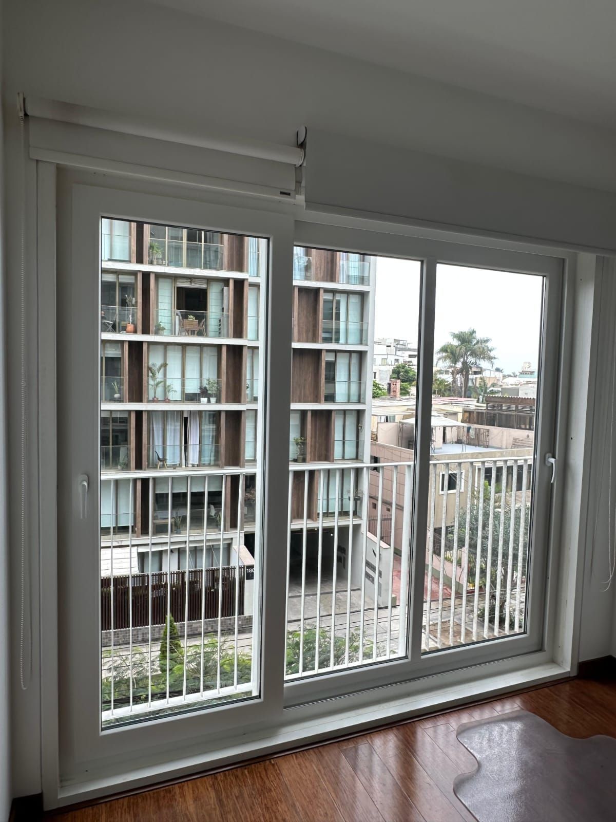 Vista desde el interior de una habitación a través de una gran puerta corrediza de cristal con marco blanco que da a un edificio de apartamentos.