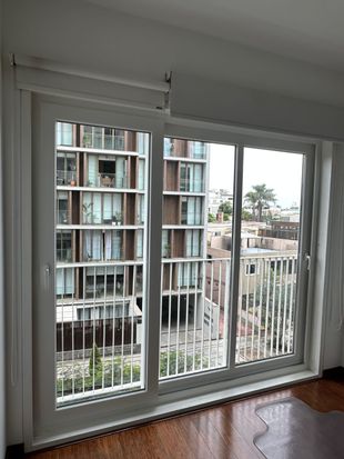 Vista desde el interior de una habitación a través de una gran puerta corrediza de cristal con marco blanco que da a un edificio de apartamentos.