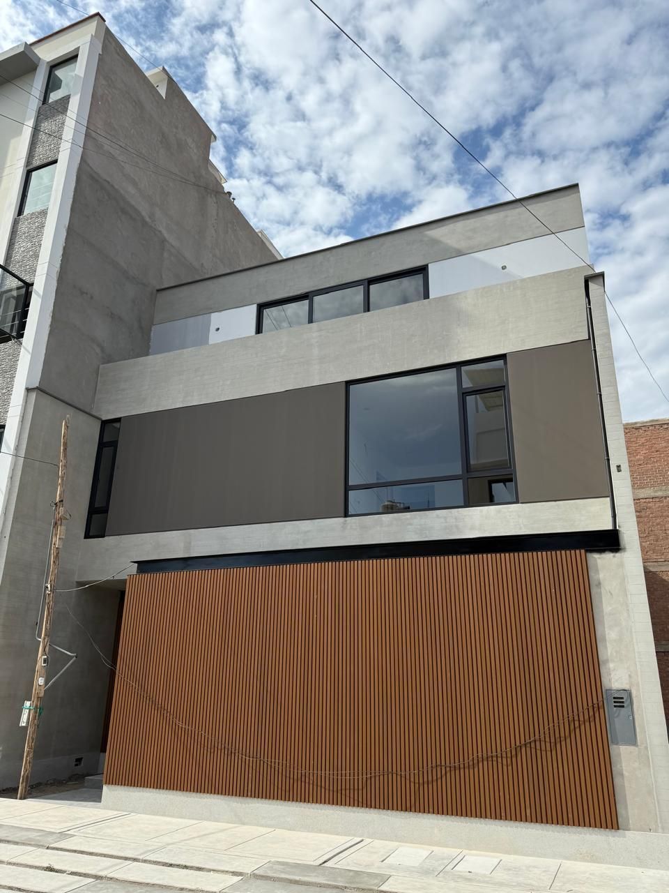 Una persona con una camisa gris instala un sistema de puertas corredizas de vidrio de gran tamaño con marco blanco en un patio embaldosado.