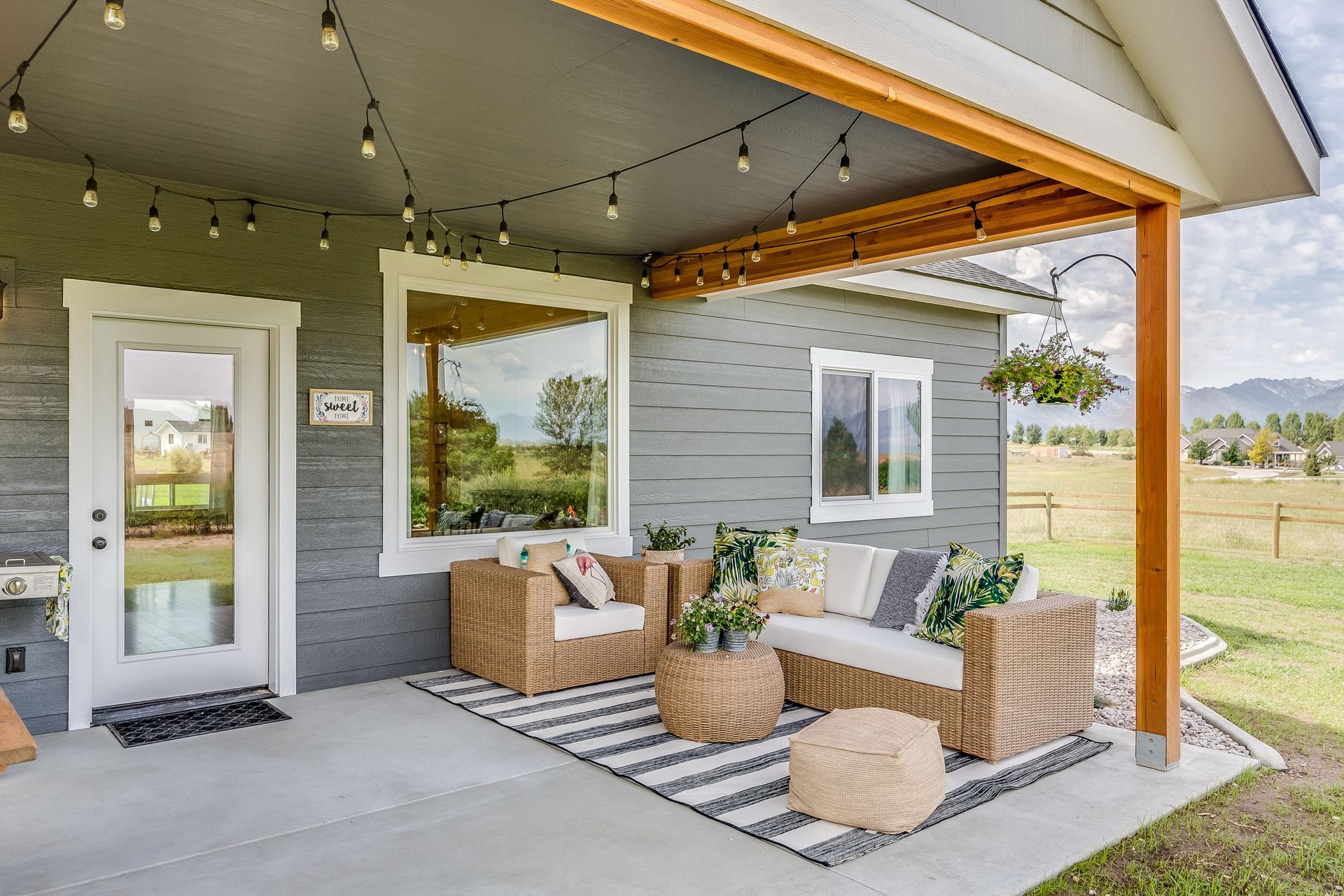 Outdoor patio with seating, string lights, gray siding, and a view of a field.