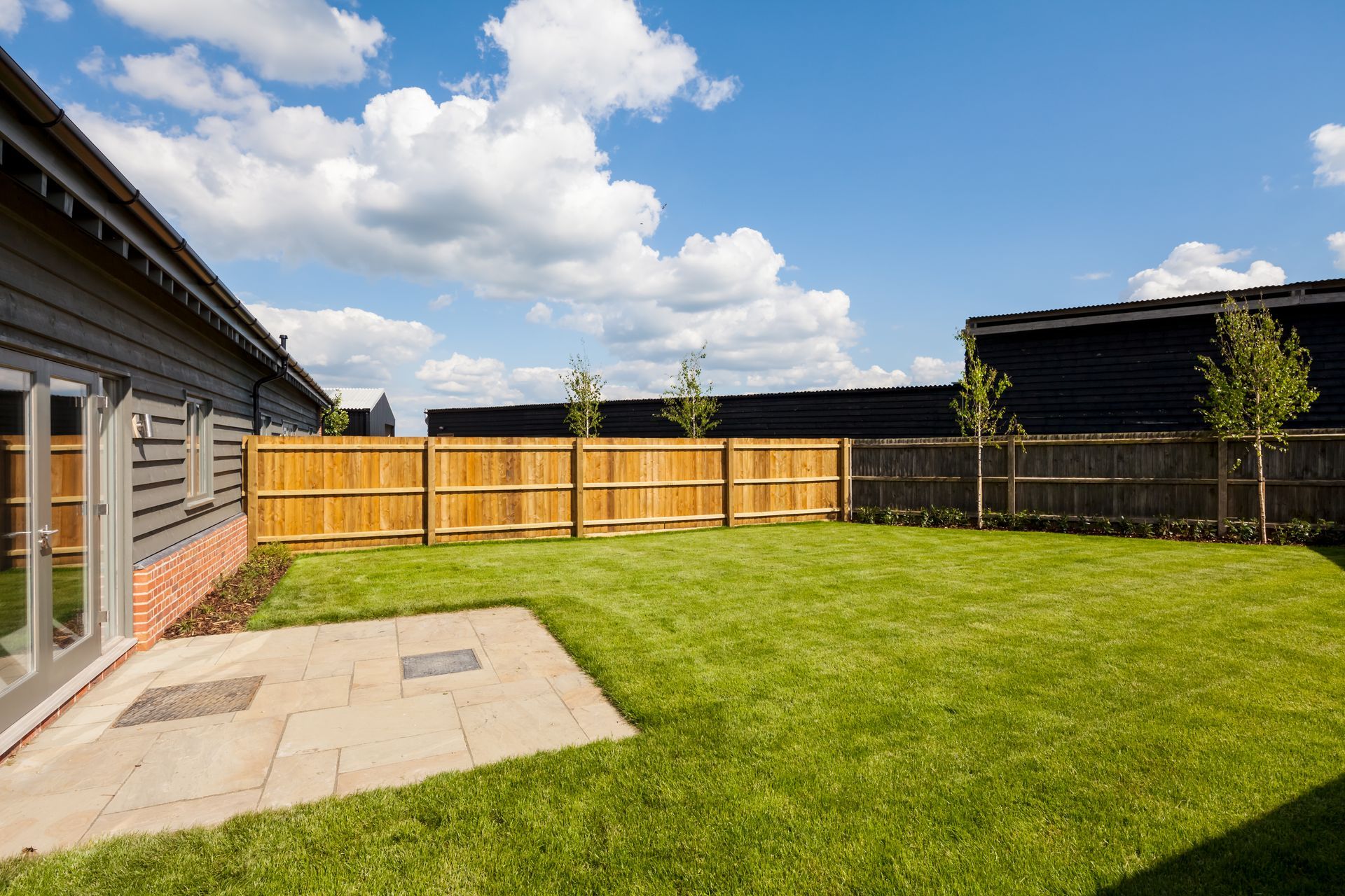 Lawn and fenced yard outside a house under a blue sky with fluffy clouds.