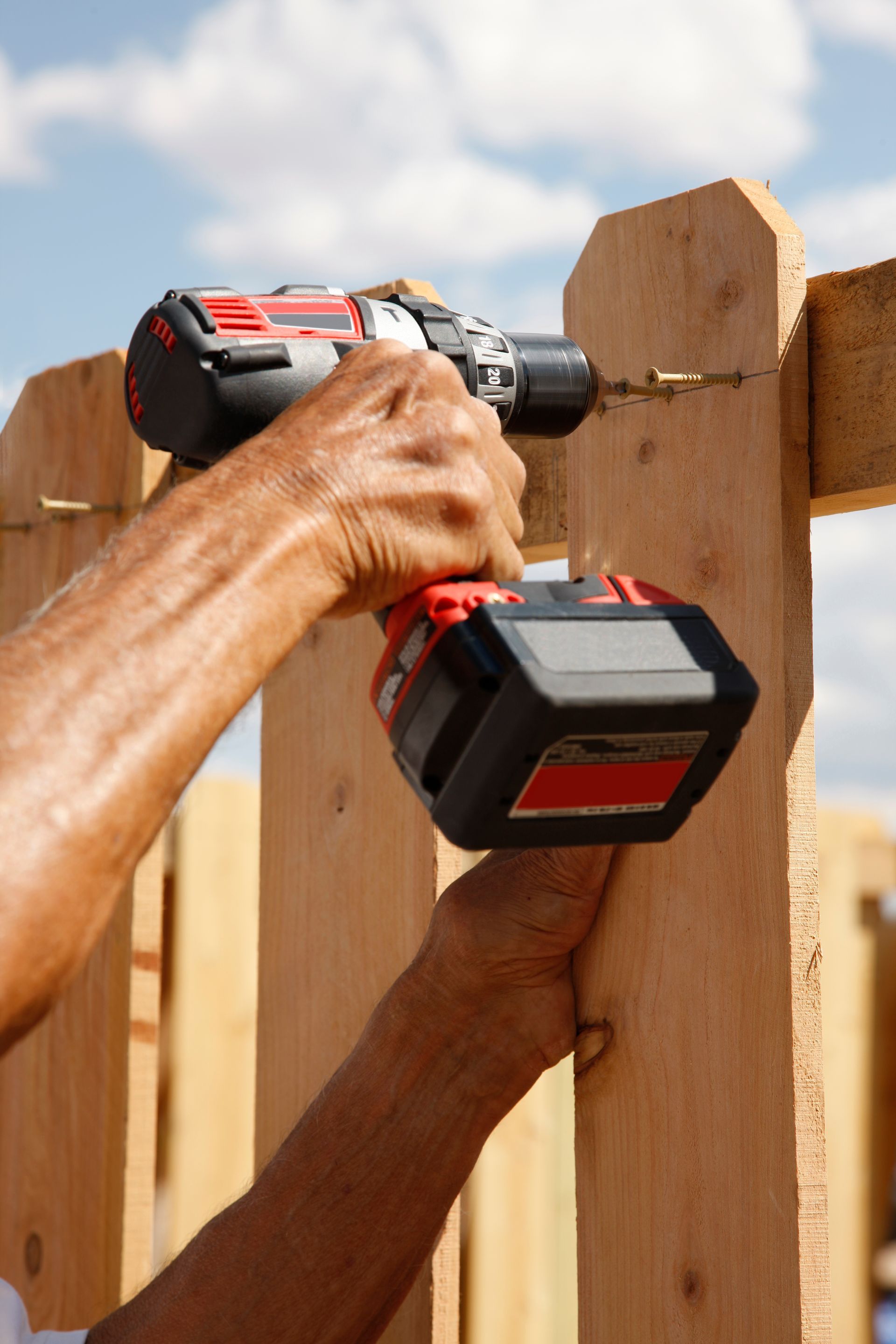 Person using a power drill to attach wood planks outdoors.