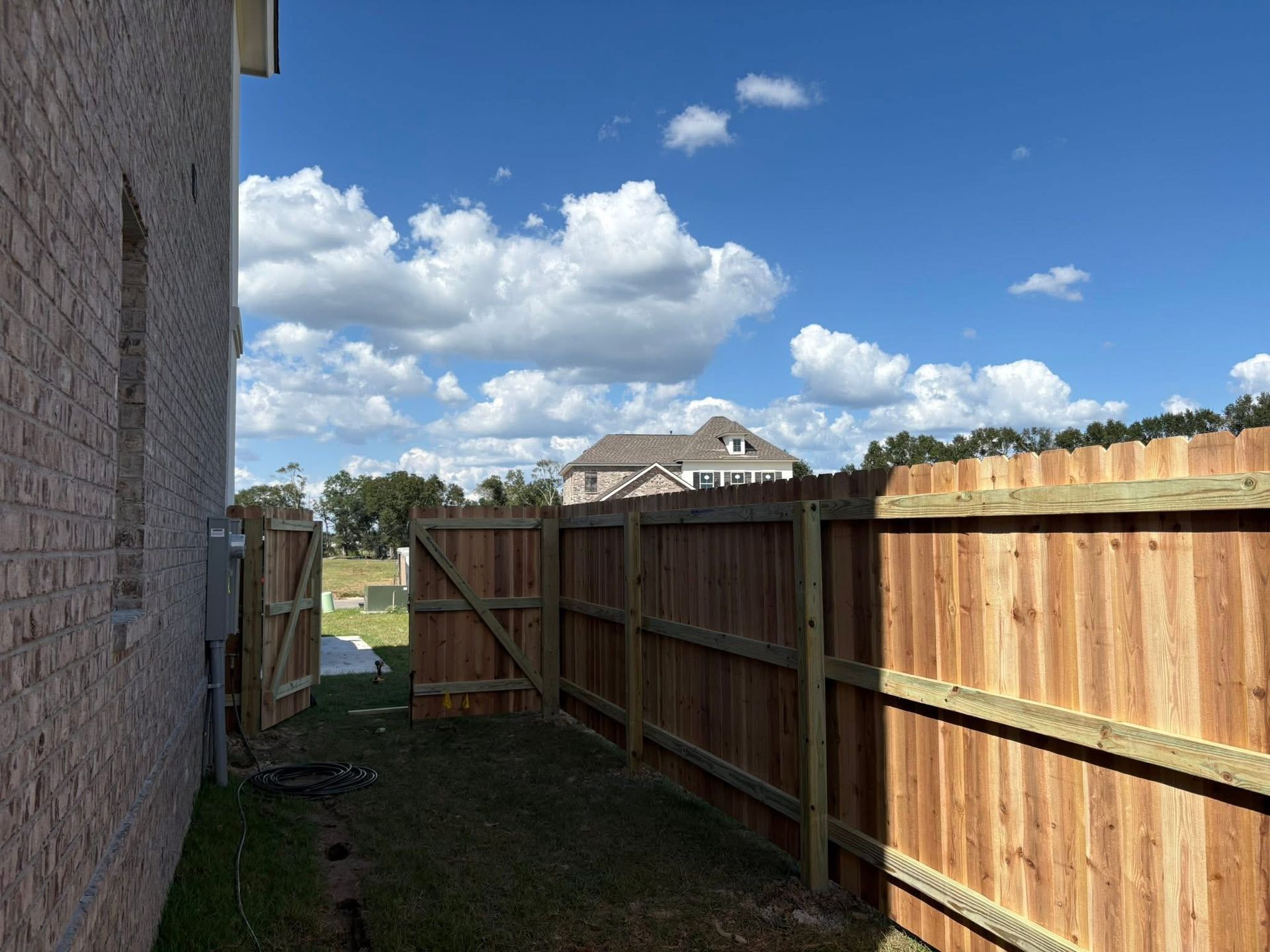 Wooden fence runs along side of a brick house, under a cloudy blue sky.