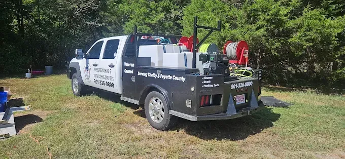 A white and black utility truck with equipment reels and water tanks parked in a grassy area with trees.