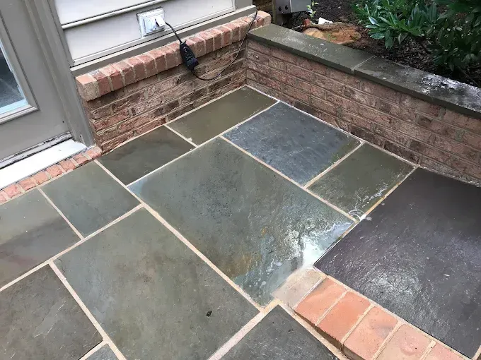 A stone patio with rectangular blue-grey flagstones and a matching red brick border near a house wall.