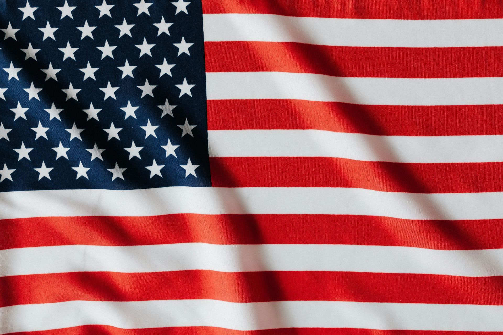 A close-up of a folded, textured American flag featuring red and white stripes and a blue canton with white stars.