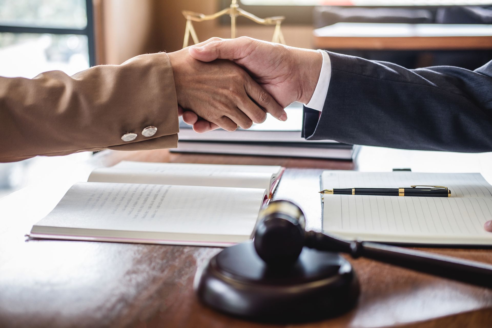 Two people shaking hands over a table with legal documents and a gavel.