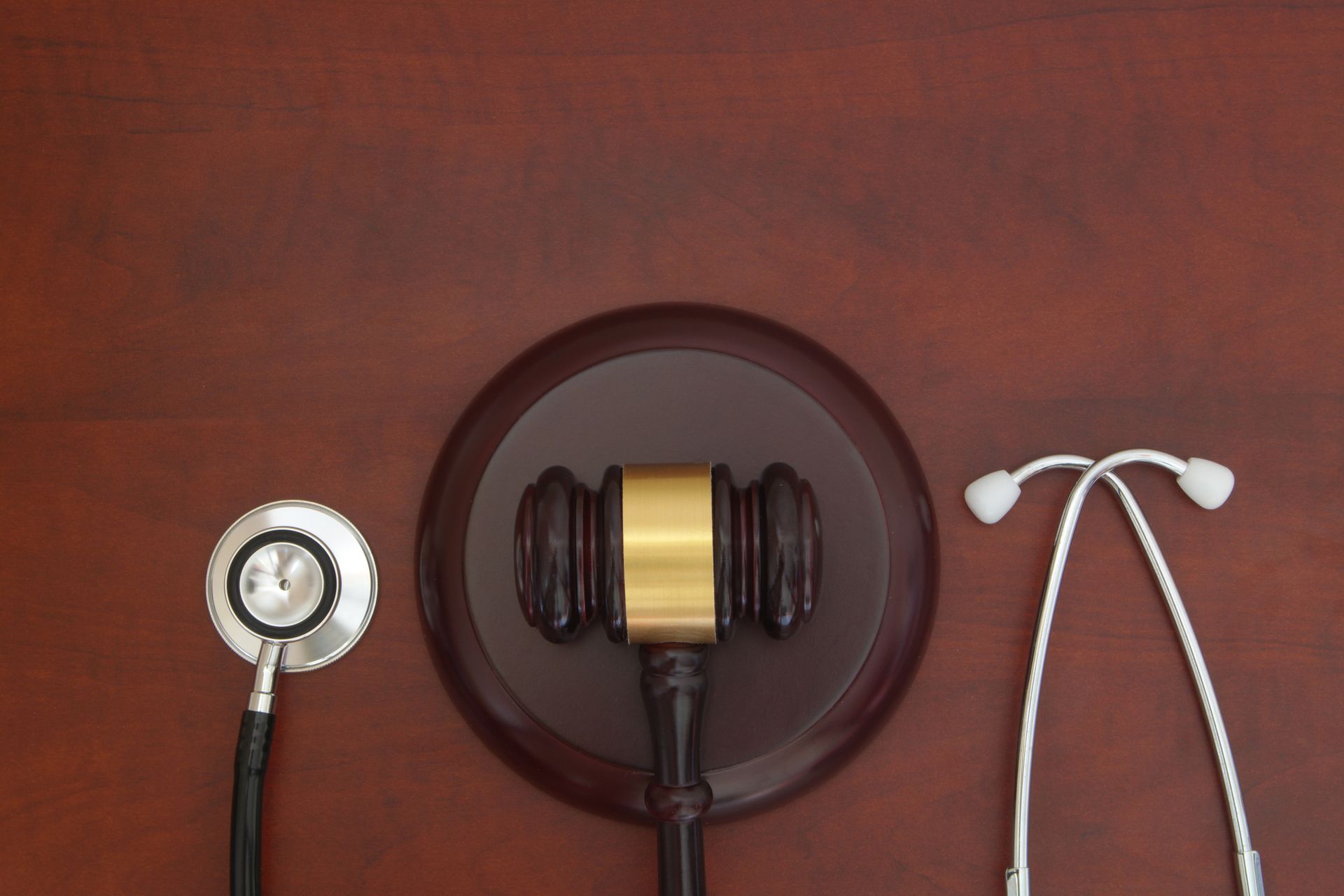 Gavel centered between a stethoscope and its two earpieces on a brown wood surface.