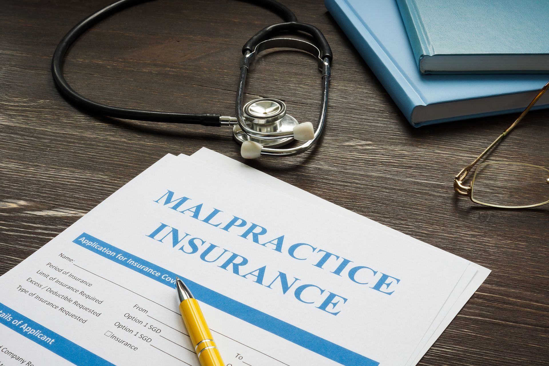 Malpractice insurance document with stethoscope, pen, glasses, and books on a wooden desk. Malpractice insurance document with stethoscope, pen, glasses, and books on a wooden desk.