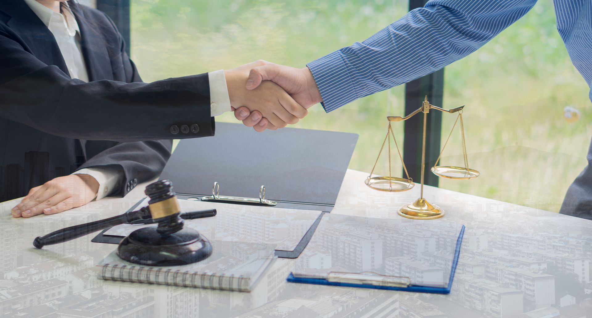 Two people shaking hands at a desk with a gavel, scales of justice, and documents. Two people shaking hands at a desk with a gavel, scales of justice, and documents.