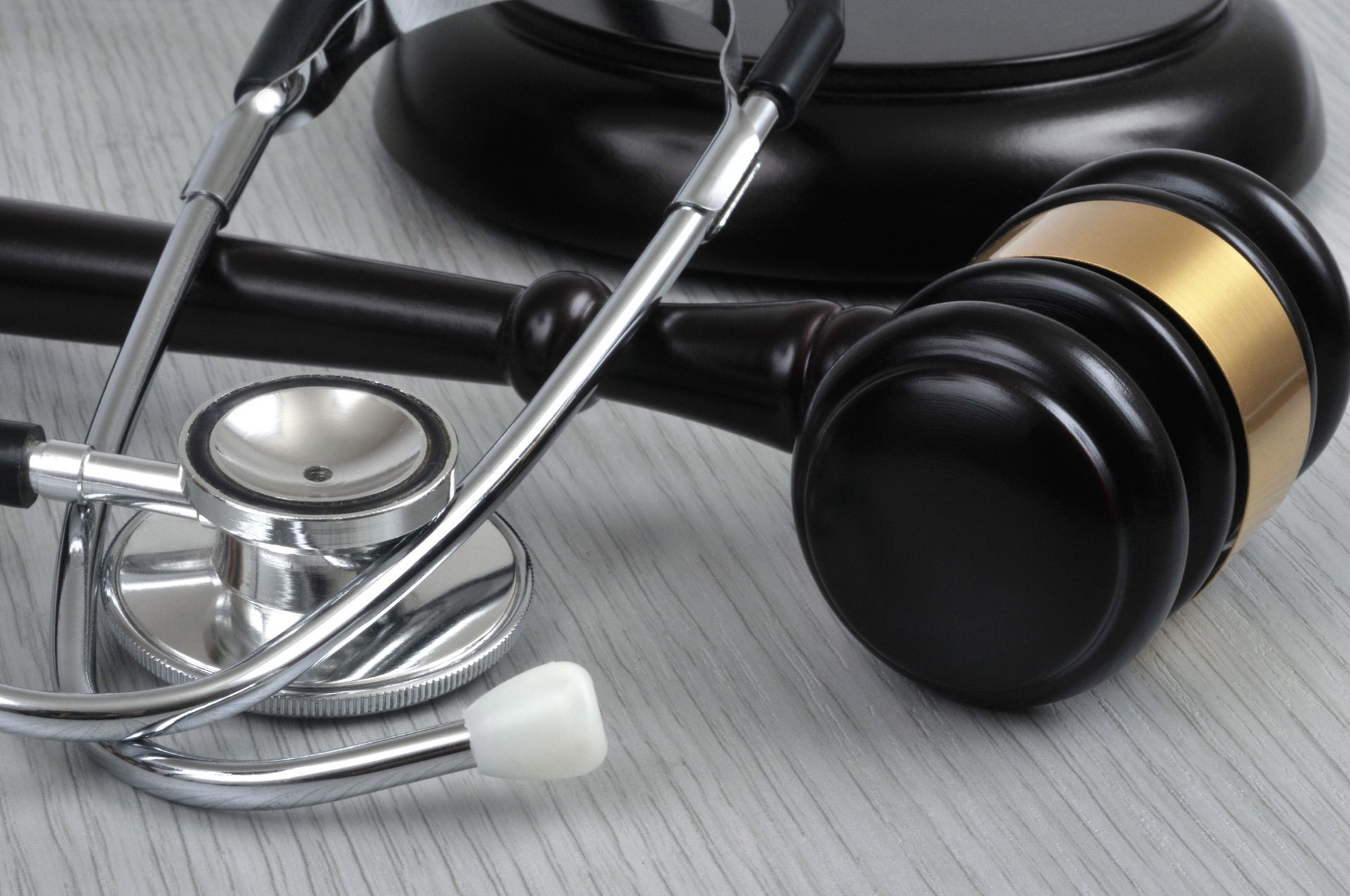 Stethoscope draped over a gavel on a light-colored surface; legal and medical tools.