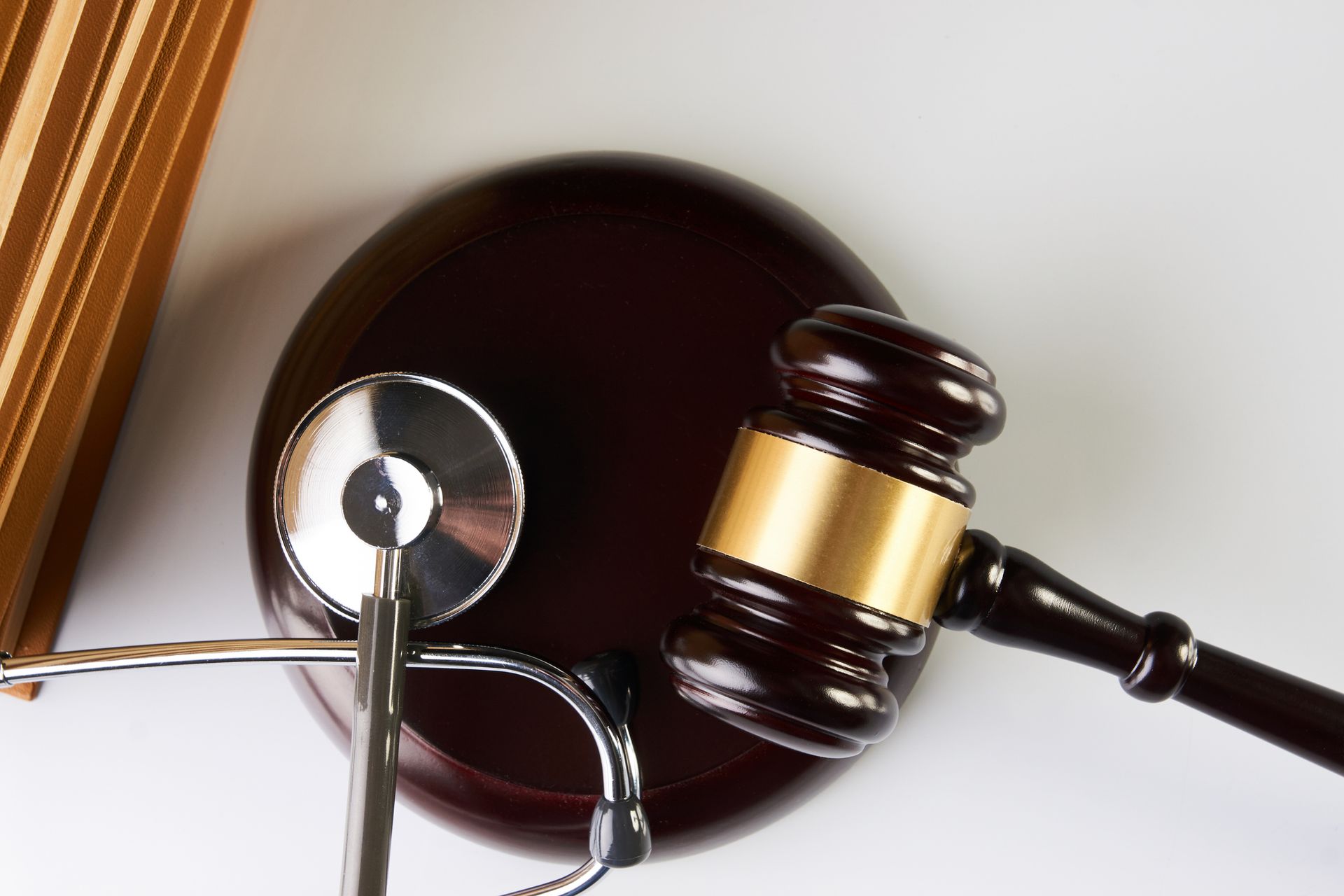Brown gavel and stethoscope on a wooden block, next to a stack of books, indicating medical law.