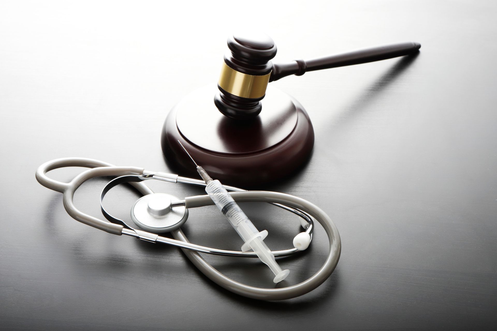 A stethoscope a syringe and a judge 's gavel on a table A stethoscope a syringe and a judge 's gavel on a table