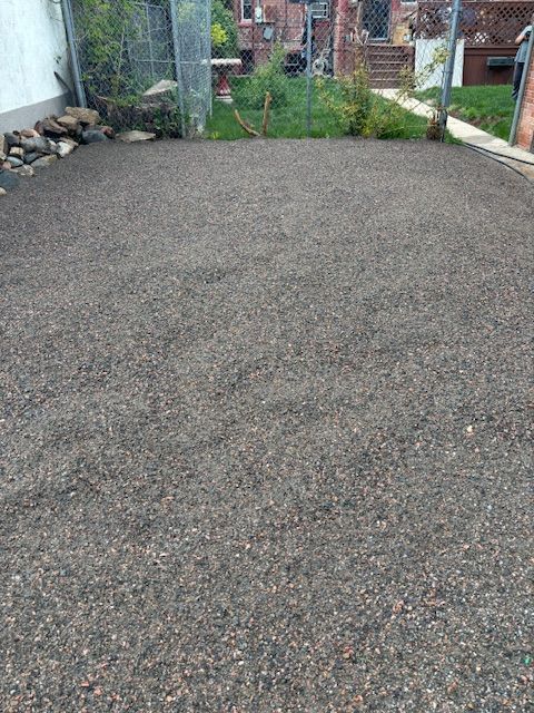 A gravel driveway in a backyard with a fence in the background.