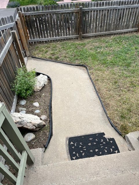 A concrete walkway leading to a fenced in yard