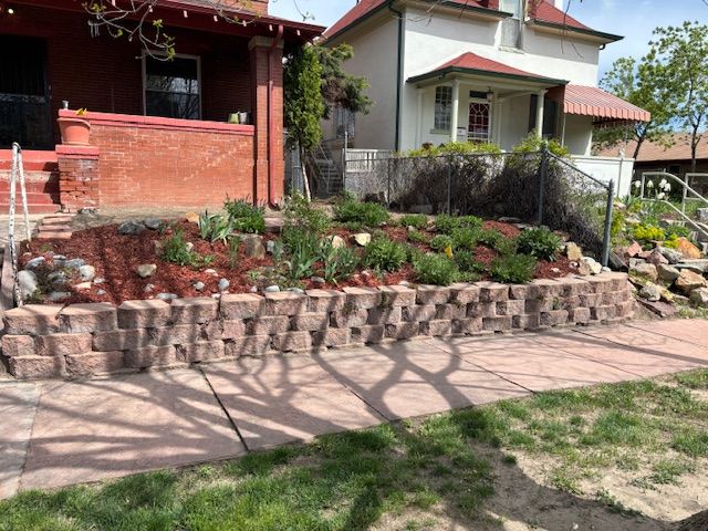 A brick wall with a lot of plants in front of a house.