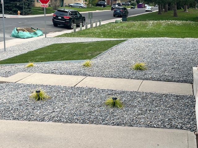 A car is parked on the side of the road in front of a gravel driveway.