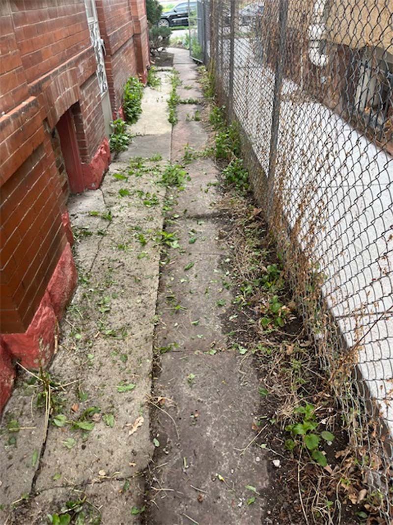 A narrow sidewalk between two buildings next to a chain link fence.
