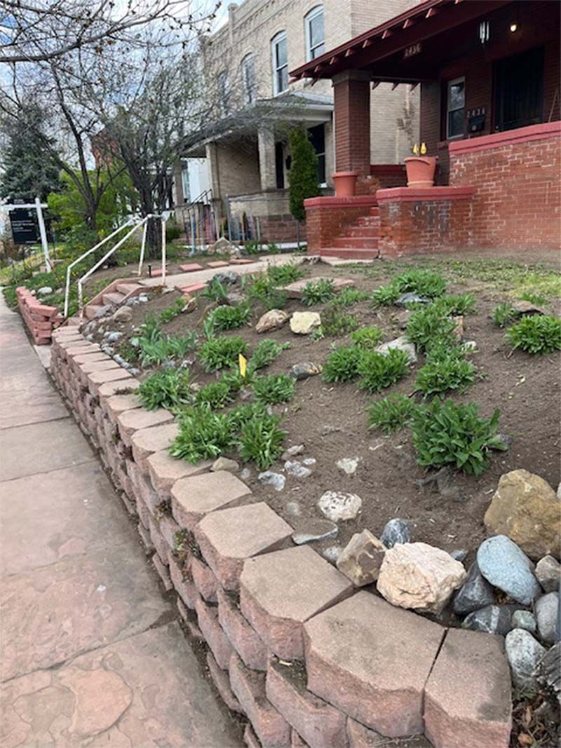 A stone wall surrounds a lush green garden in front of a house.