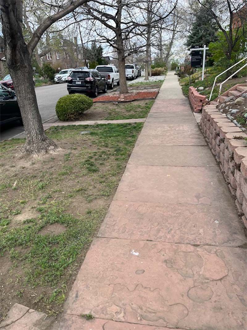 A sidewalk in a residential neighborhood with cars parked on the side of it.