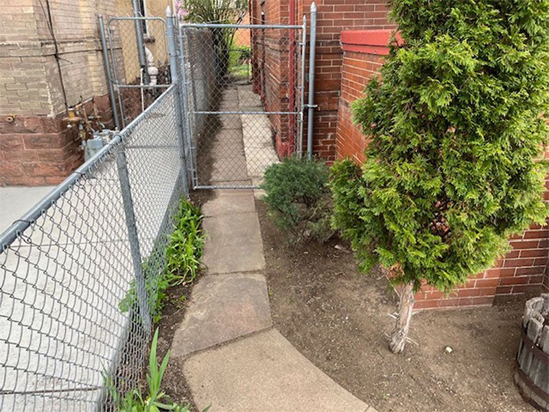 A chain link fence surrounds a sidewalk leading to a brick building.