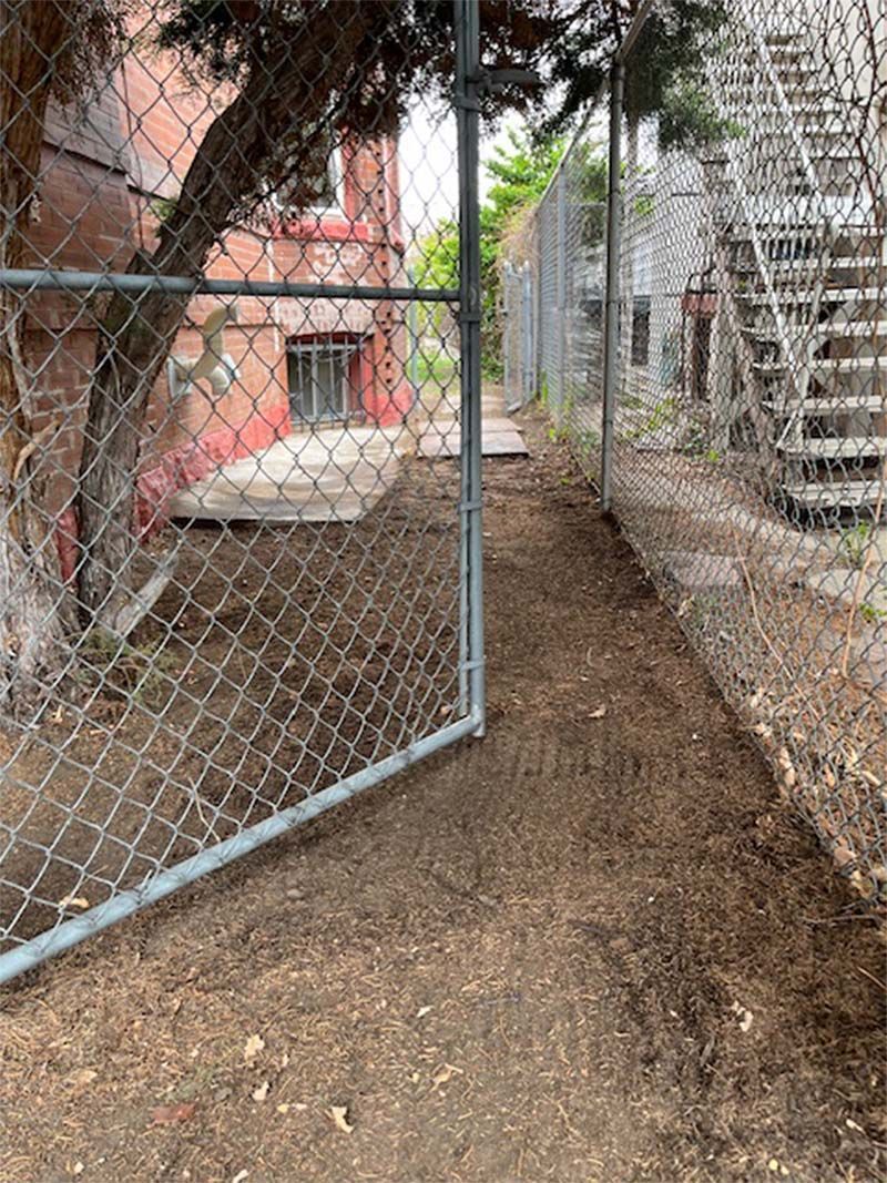 A chain link fence surrounds a dirt path leading to a building.
