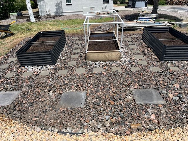 Three raised beds in a gravel area in front of a house