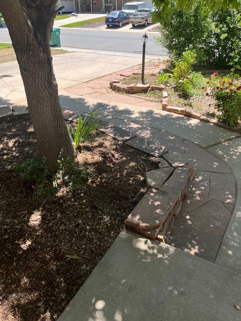 A sidewalk with a tree in the background and a car parked on the side of the road.