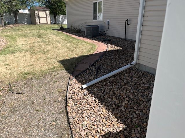 A drain pipe is sitting on the side of a house next to a sidewalk.