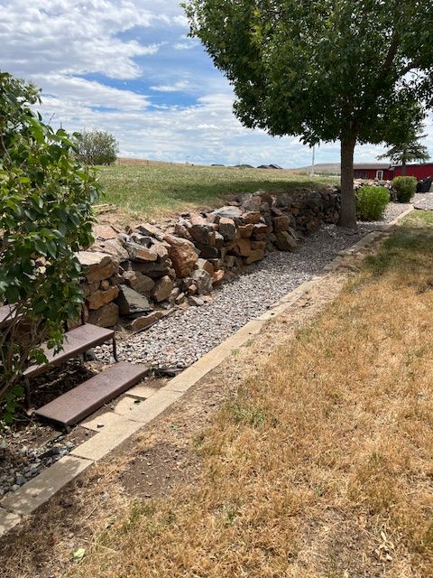 A stone wall with a picnic table and a tree in the background