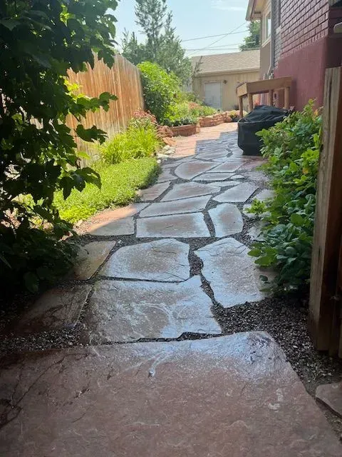 A backyard with a brick walkway and a white house in the background