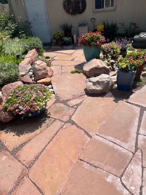 A stone patio with flowers and rocks in front of a house.